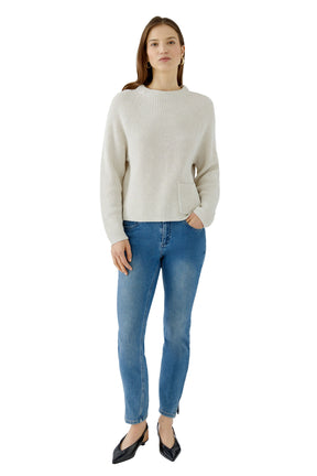 Women's full-length front model view of cream rib-knit crewneck long-sleeve knit sweater with one front patch pocket by Oui