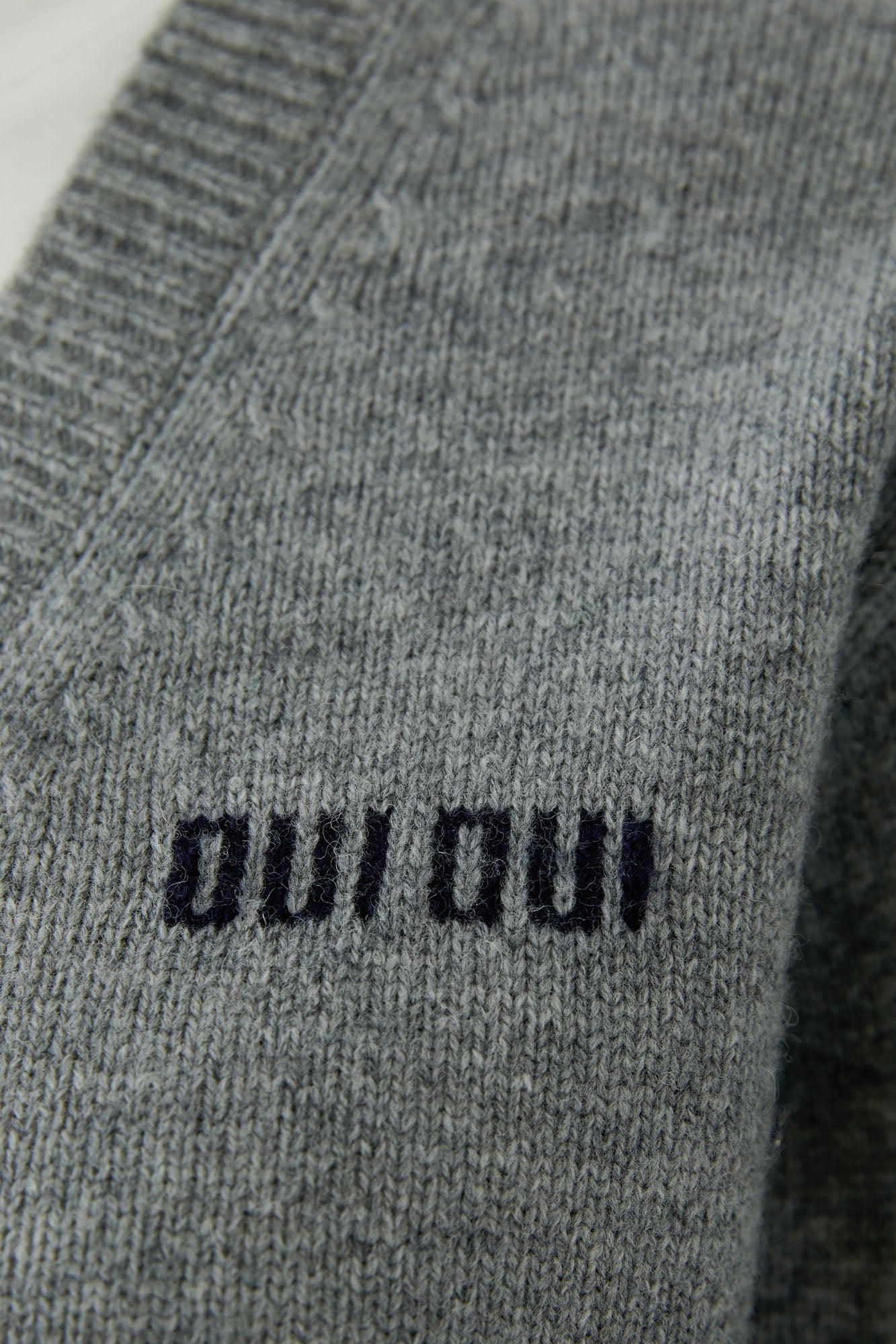 Women's gray knit long-sleeve knit sweater texture with black “oui oui” chest text and ribbed V-neck seam, close-up