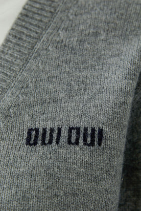 Women's gray knit long-sleeve knit sweater texture with black “oui oui” chest text and ribbed V-neck seam, close-up