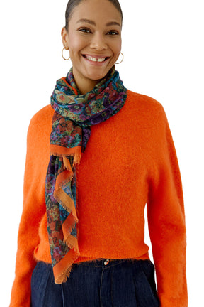 Oui women's multicolor floral scarf with orange border and fringe worn over an orange sweater shown from the front