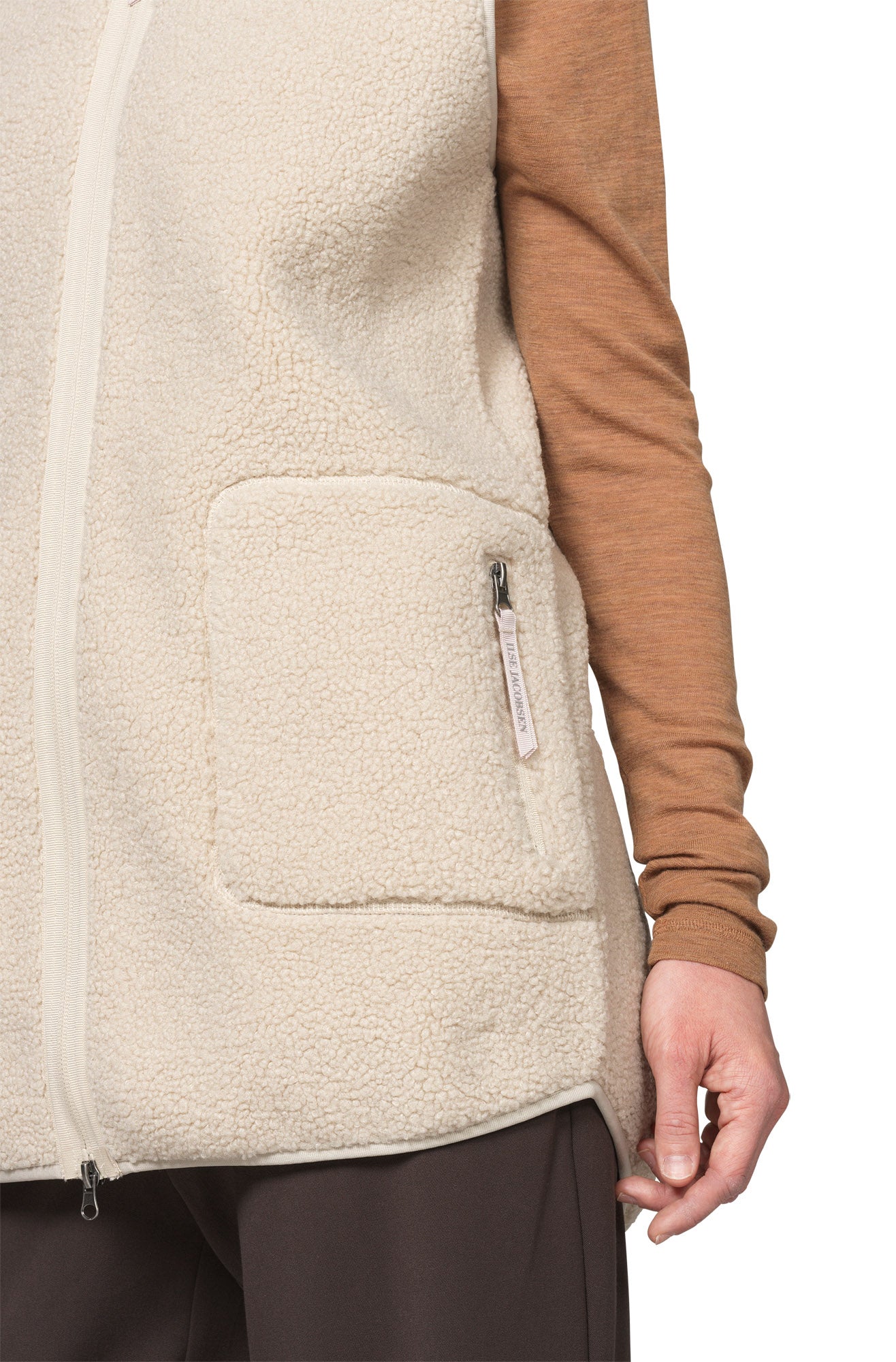 Women's detail of cream curly fleece vest pocket with vertical zipper pull beside a brown sleeve by Ilse Jacobsen