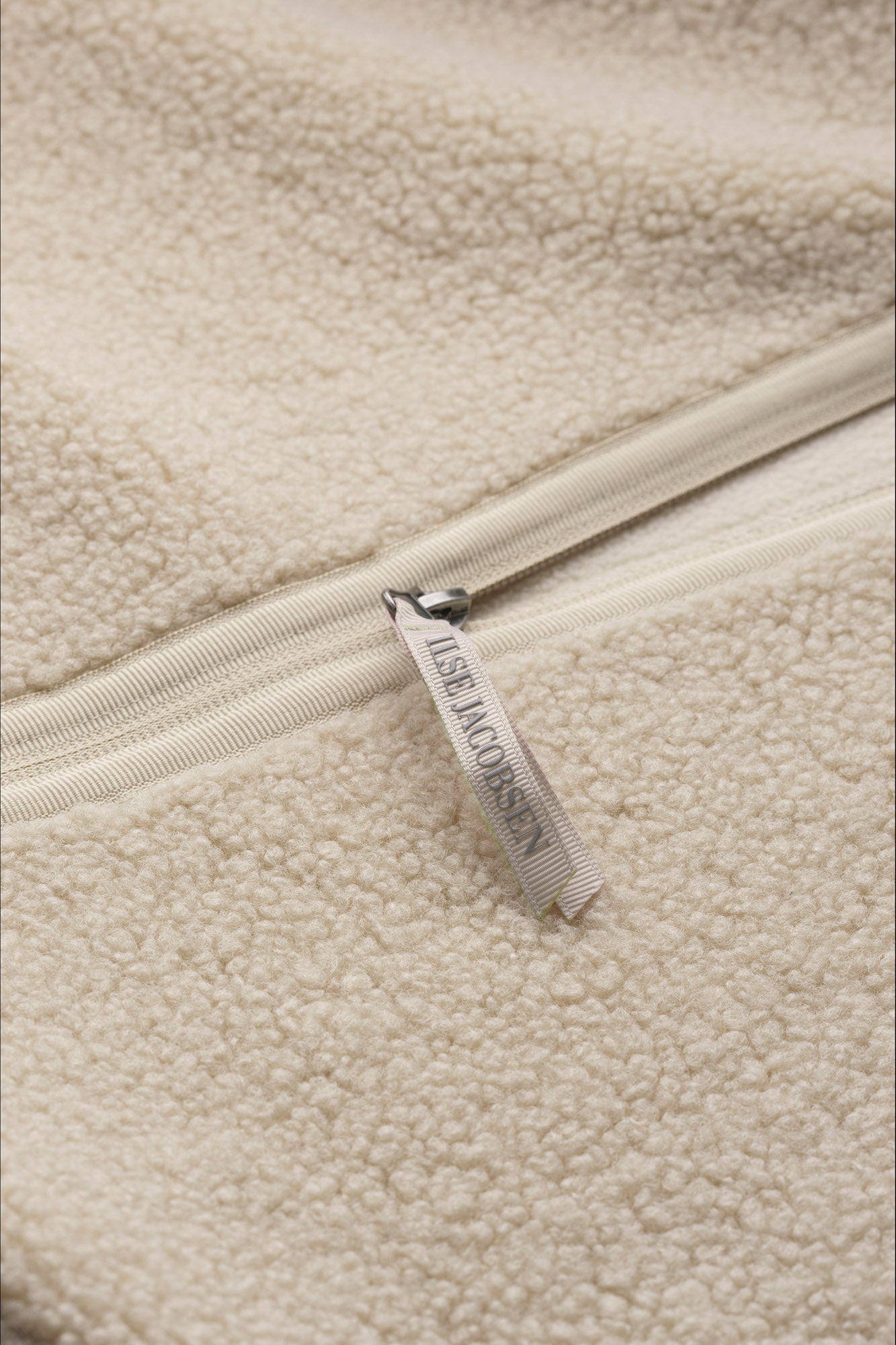 Women's detail of cream curly fleece vest pocket with vertical zipper pull beside a brown sleeve by Ilse Jacobsen