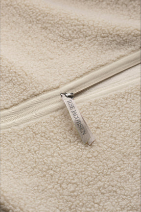 Women's detail of cream curly fleece vest pocket with vertical zipper pull beside a brown sleeve by Ilse Jacobsen