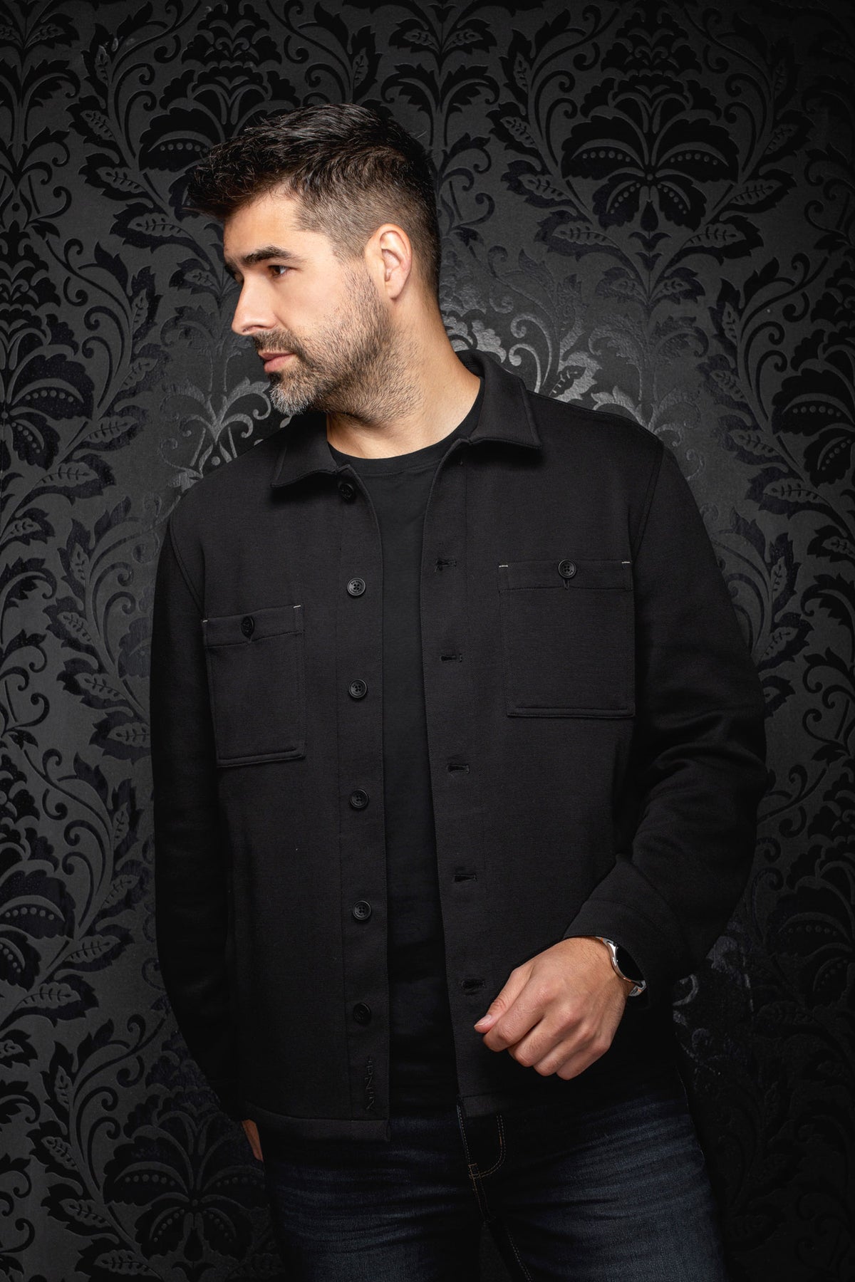 Sur mannequin de face, la surchemise noire avec col, patte boutonnée et poches poitrine pour homme par Au Noir