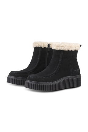 Women's black ankle boots angled front view with cream plush cuff, side zipper, and ribbed sole by Ilse Jacobsen