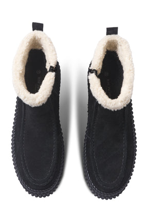 Women's black ankle boots angled front view with cream plush cuff, side zipper, and ribbed sole by Ilse Jacobsen