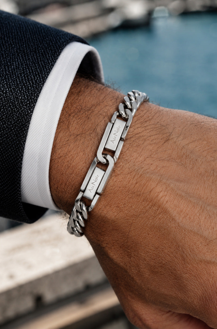 Détail: Bracelet gourmette argenté porté au poignet, avec deux plaques rectangulaires gravées Au Noir pour homme