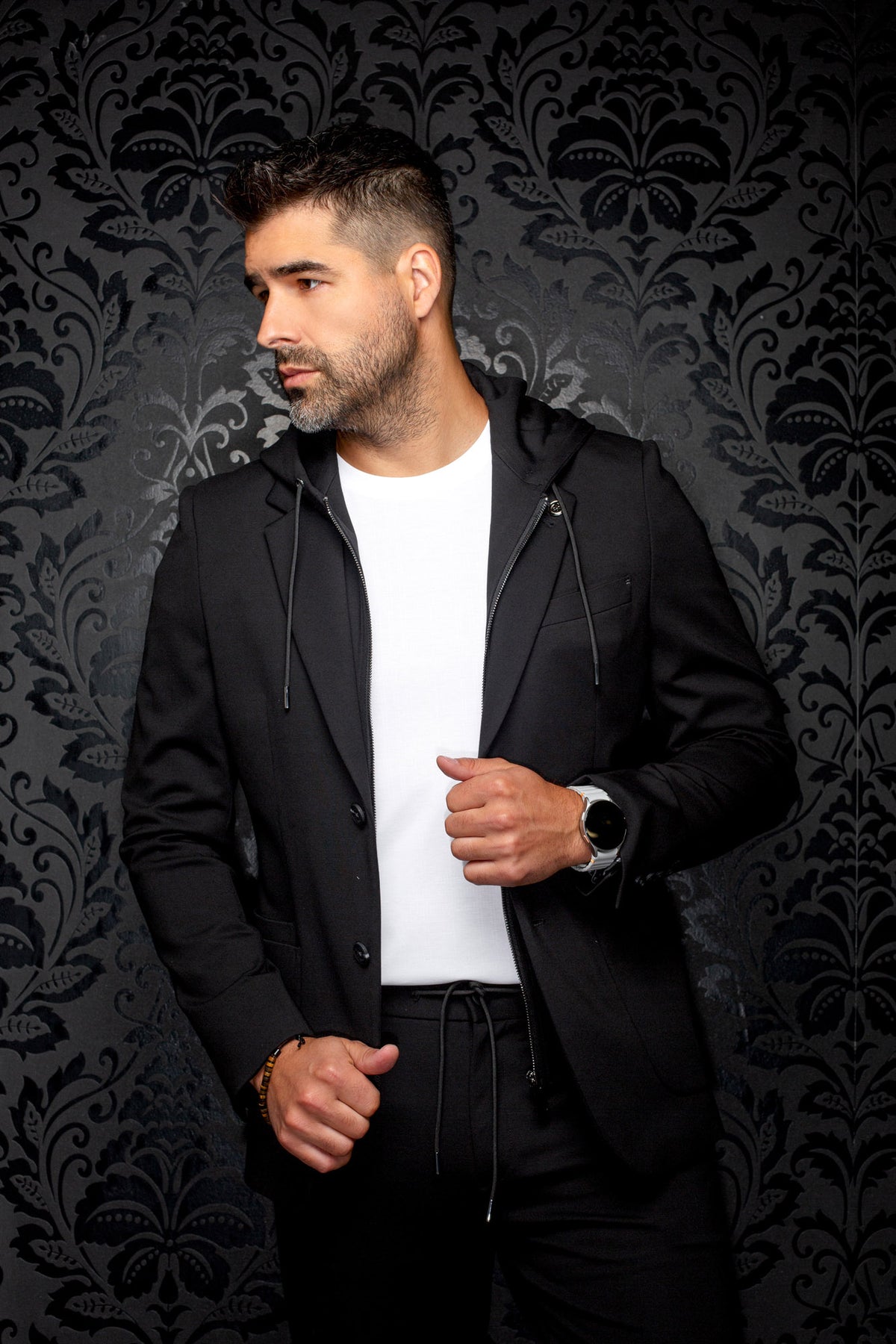 Veston noir à capuchon en vue de biais avec revers crantés, cordons et insert zippé, vue de cote pour homme par Au Noir
