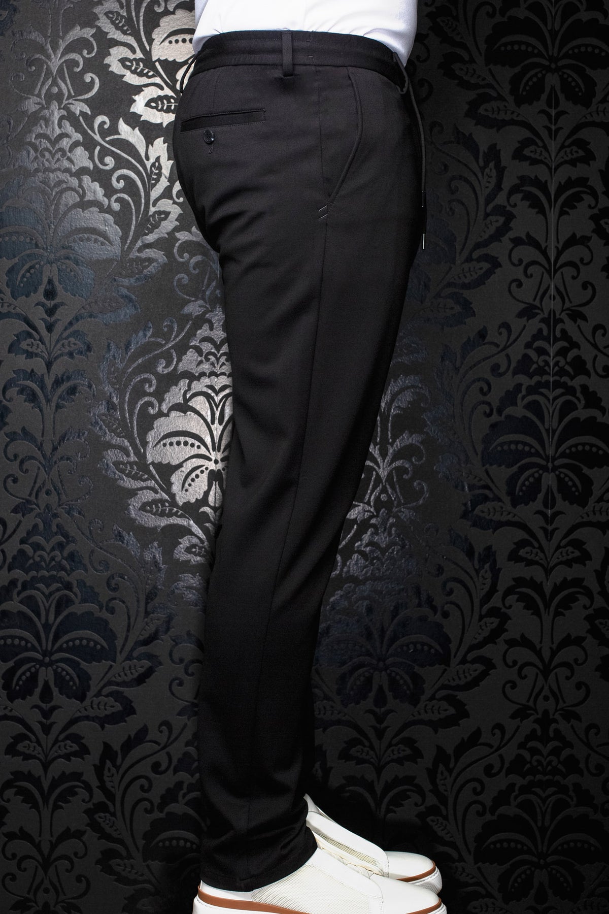 Pantalon noir vu de côté avec jambe fuselée, poche arrière passepoilée boutonnée et passants pour homme par Au Noir
