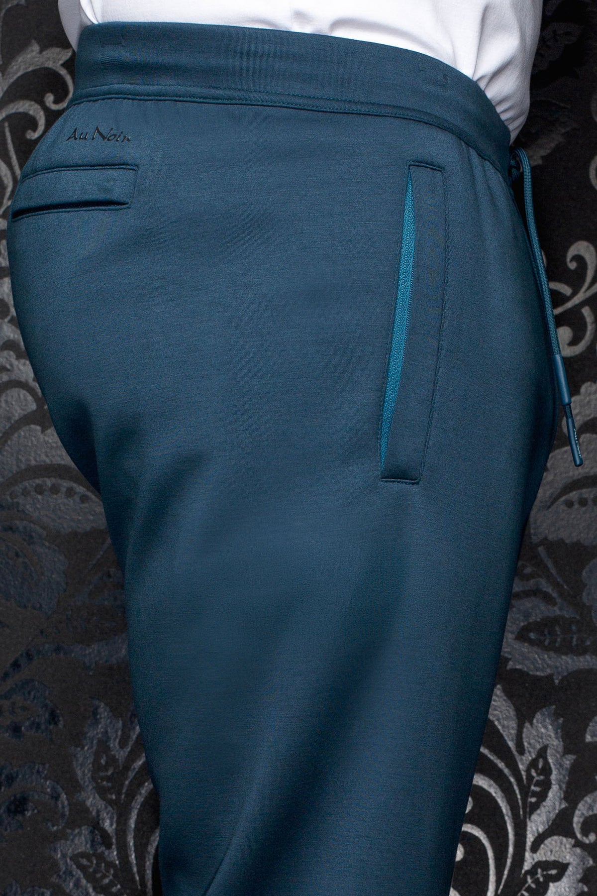 Men's teal jogging pants with Au Noir logo, back welt pocket and elastic waistband, close-up