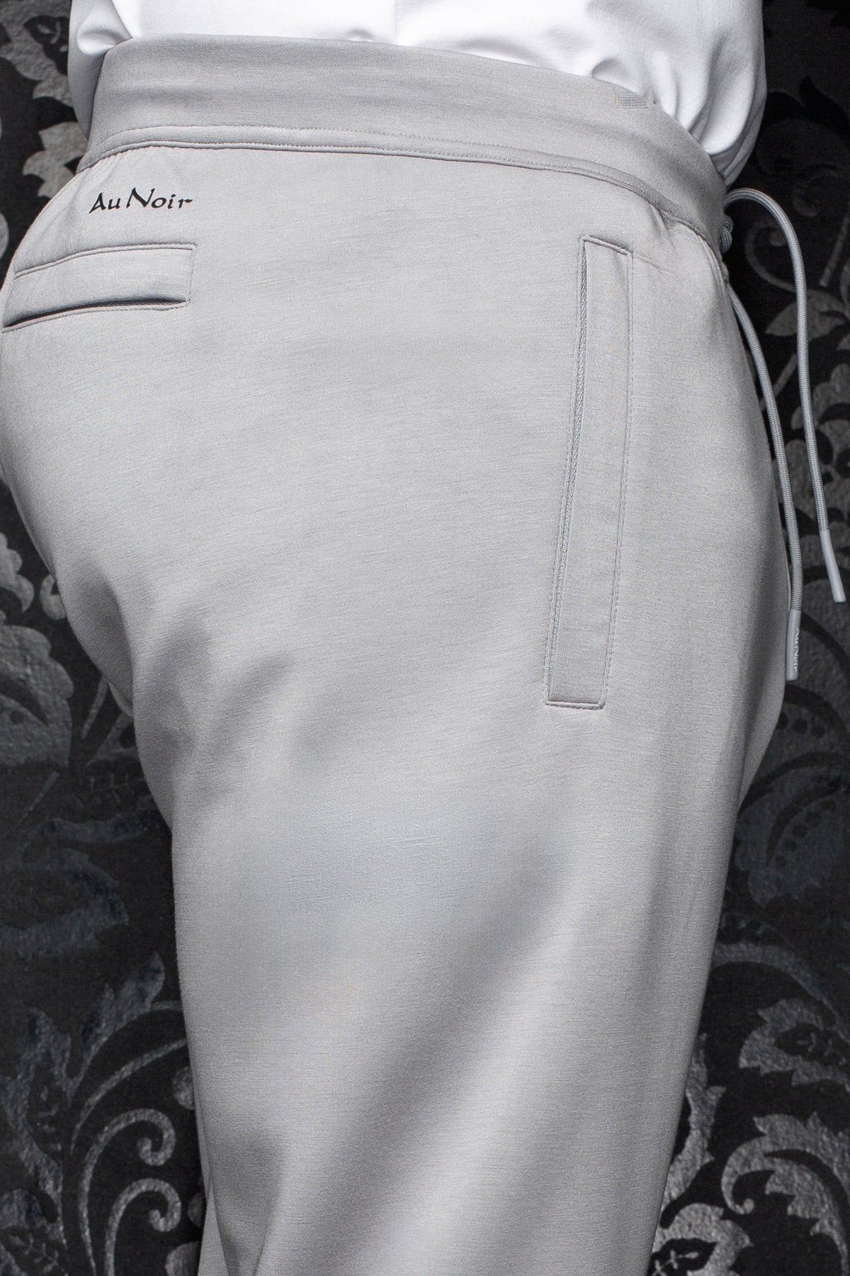 Men's light gray jogging pants waistband, small black Au Noir logo, welt pockets and drawcord, close-up