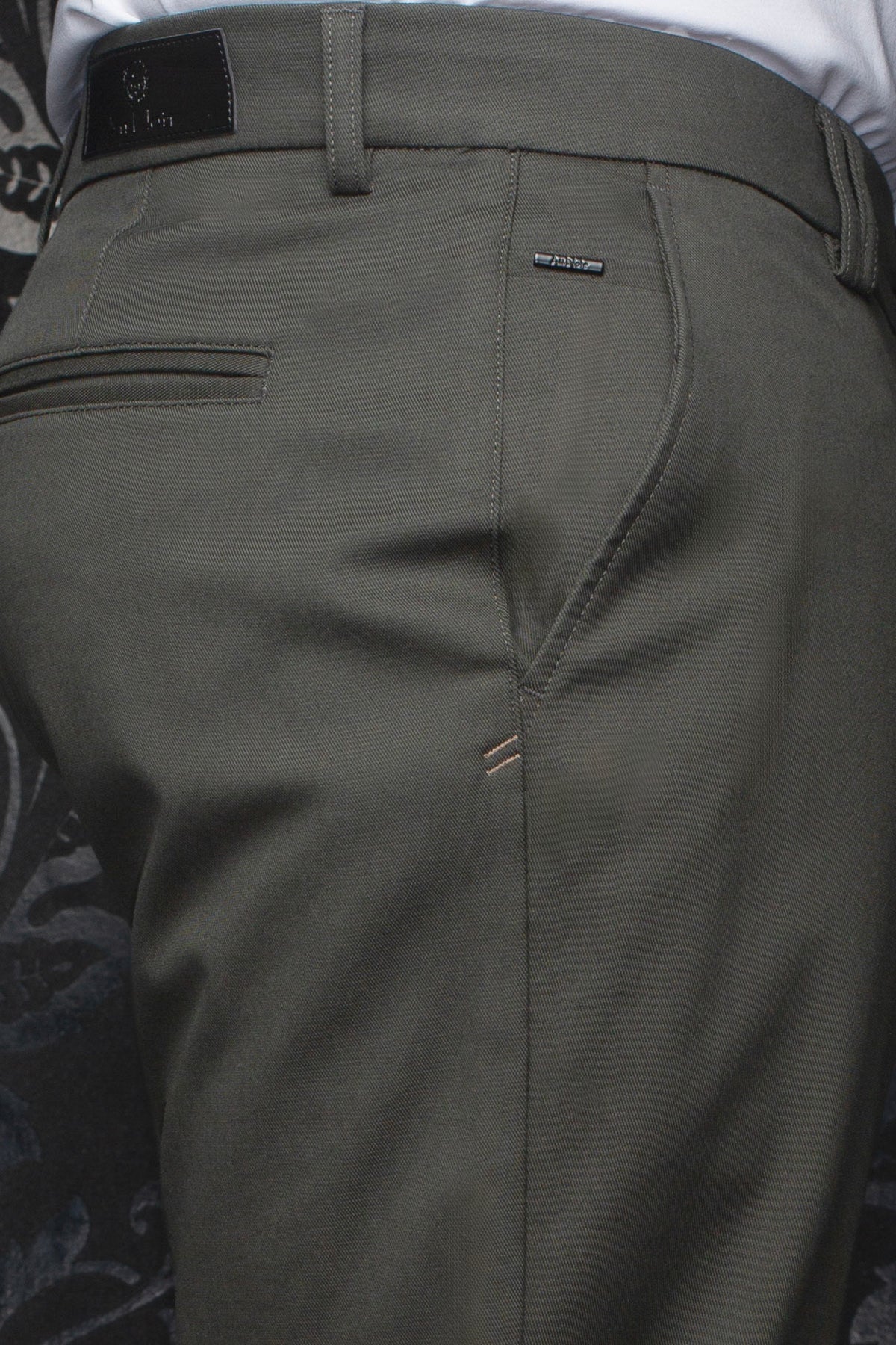 Gros plan d’un pantalon chino vert olive avec garnitures logo, poche passepoilée et passants pour homme par Au Noir