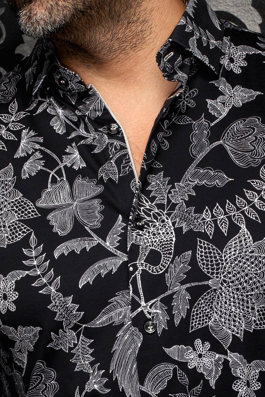Gros plan du col et de la patte d’une chemise noire à motif floral blanc et boutons noirs pour homme par Au Noir