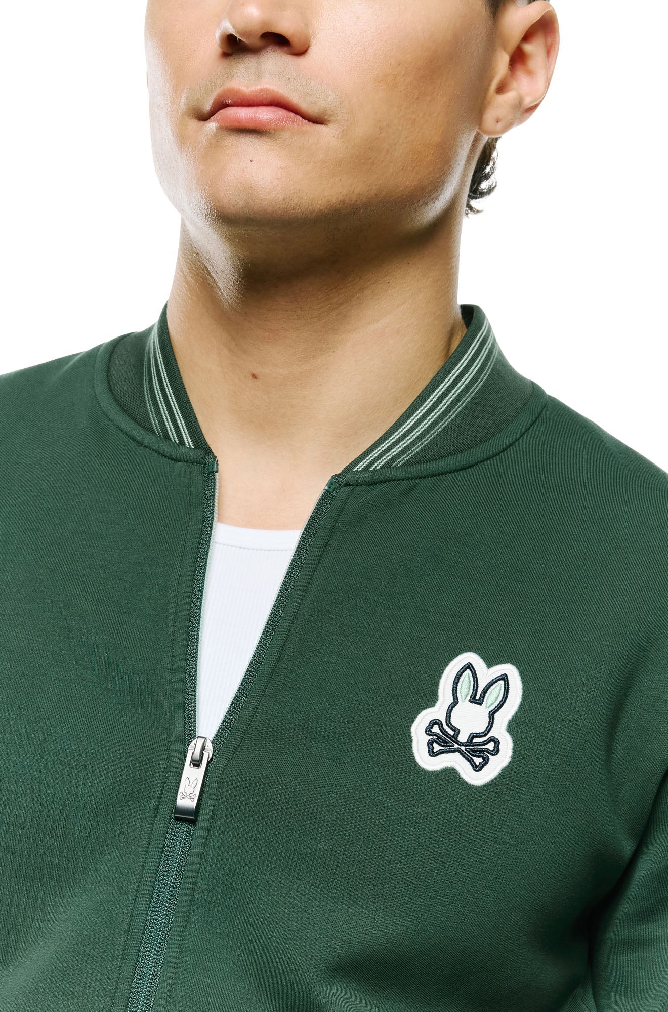 Psycho Bunny men's dark green bomber jacket collar, zipper pull and bunny skull chest patch, close-up