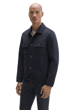 Men's angled front view of dark navy trucker jacket with button placket, flap pockets, and straight hem by Robert Barakett