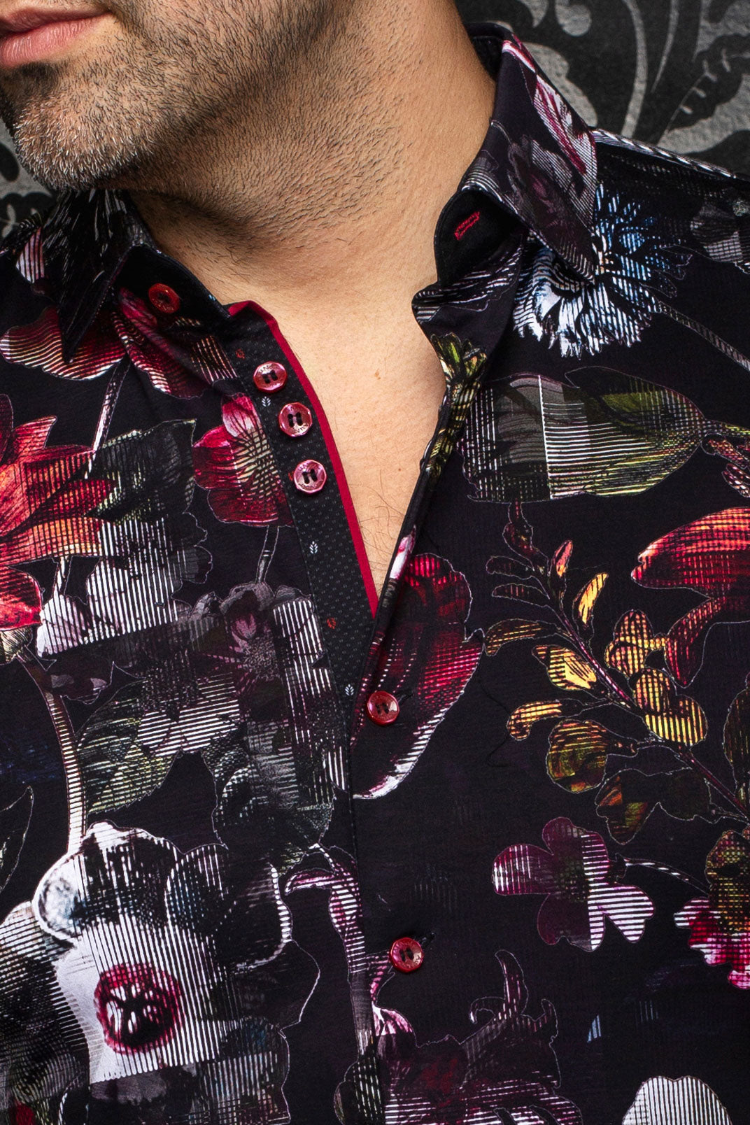 Gros plan du col d'une chemise noire fleurie, patte contrastante et boutons rouges pour homme par Au Noir