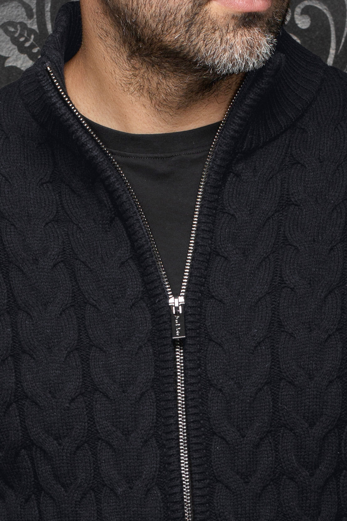 Gros plan de la veste en mérinos noire en tricot câblé avec fermeture argentée et col côtelé pour homme par Au Noir