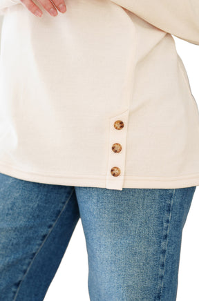 Rien ne se perd, tout se crée women's cream tunic hem with side placket and three tan buttons over blue jeans, close-up