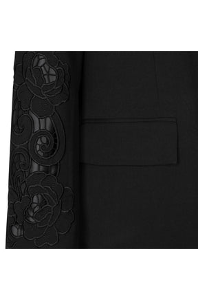 Détail du veston noir avec broderie florale ajourée sur la manche et poche à rabat pour femme par Esqualo