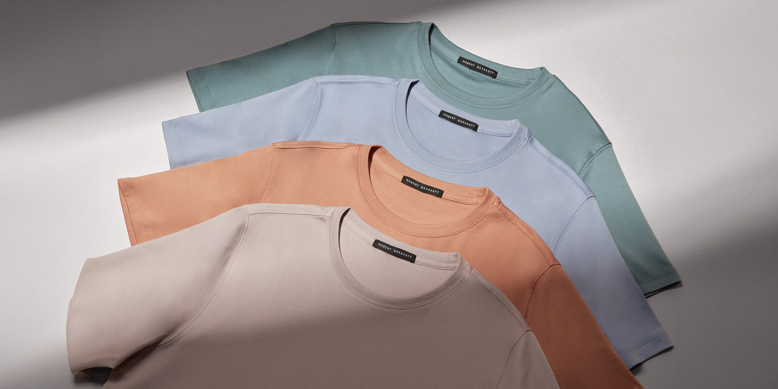 Quatre T-Shirts Robert Barakett à col rond superposés dans des teintes pastel de beige, orange, bleu et vert.
