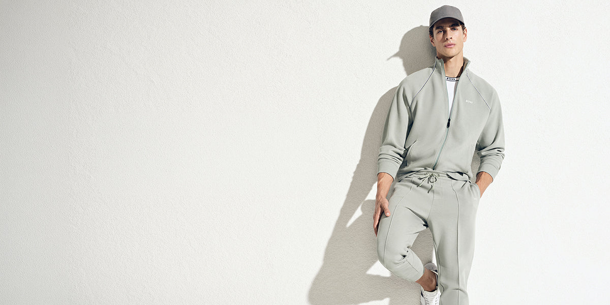 Ensemble BOSS gris clair composé d’une veste zippée et d’un pantalon assorti, avec casquette et chaussures sport blanches.
