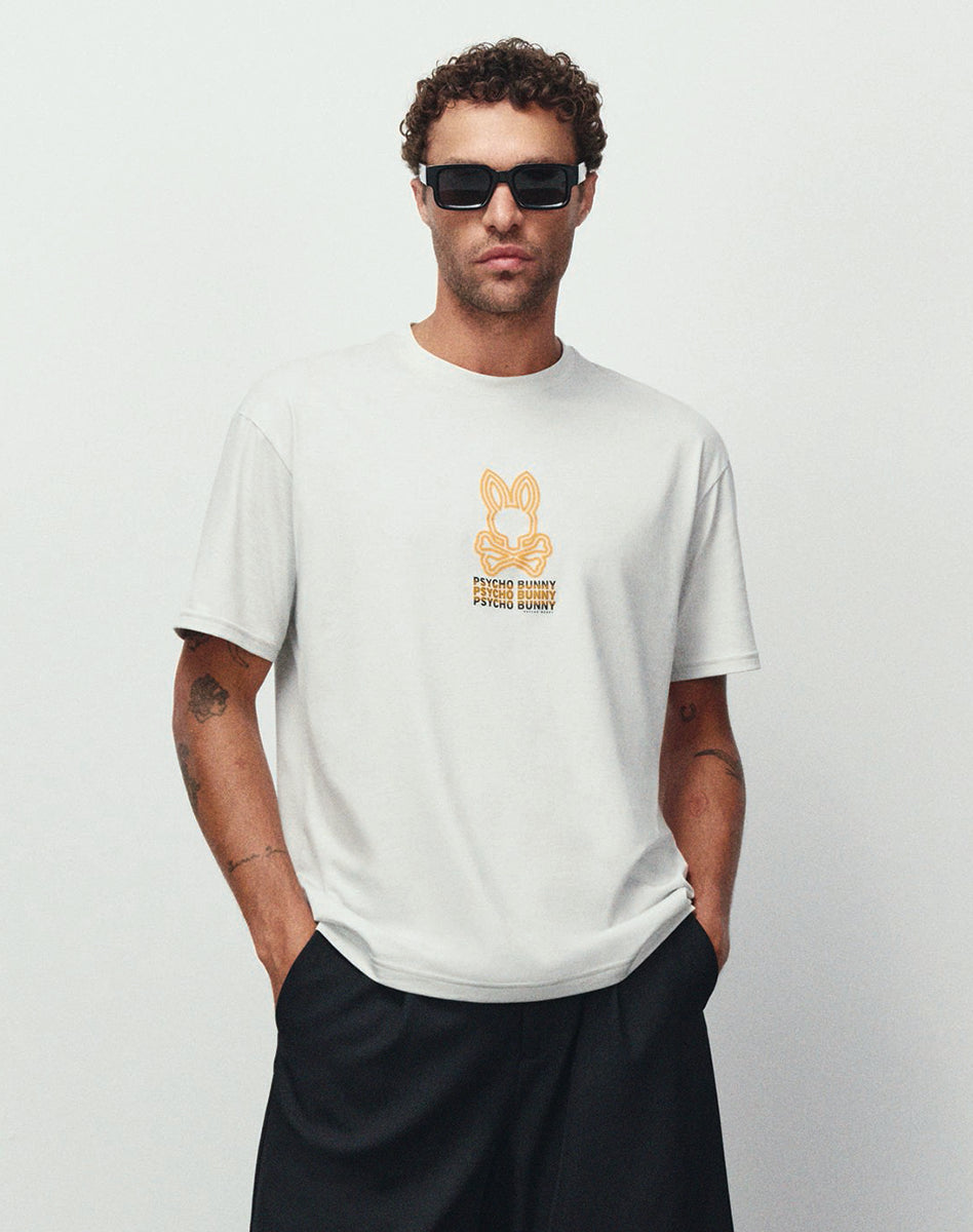White Psycho Bunny T-Shirt featuring an orange graphic logo on the chest, styled with black pants and sunglasses.