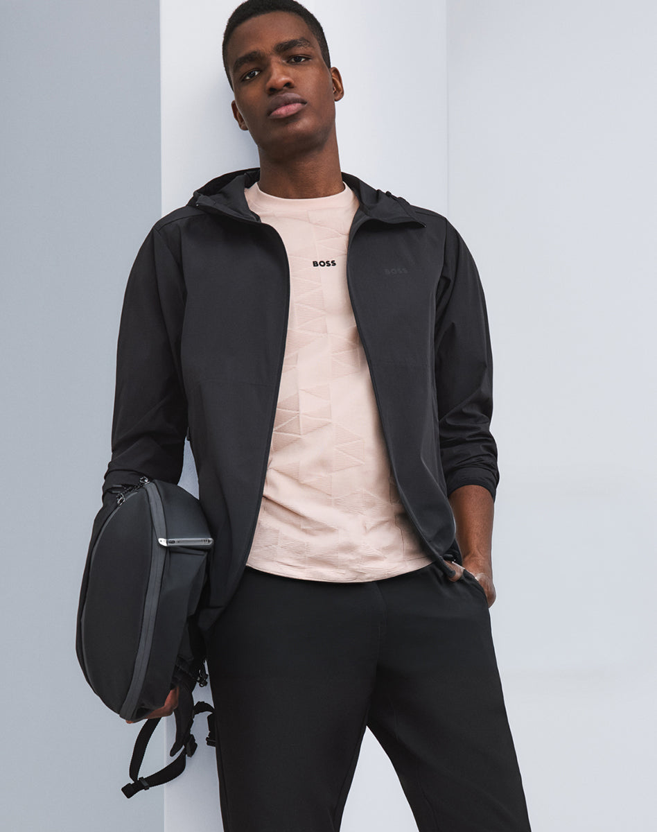 Black hooded Vest layered over a textured light pink T-Shirt, paired with black pants and a bag.